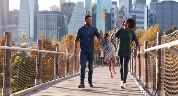 family walking on footbridge in front of cityscape