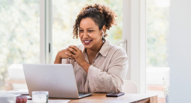 A Black woman sits at her desk and smiles at her computer while she looks at how to start a new career.