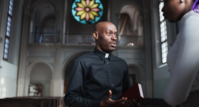 A clergyman, one of the most fulfilling jobs, talks to a Black woman in a church, indicating he’s helping her find purpose in life.