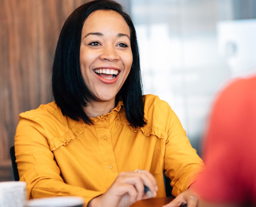 A women during a meeting smiles while speaking to another women, indicating she's learned how to ask for a raise.