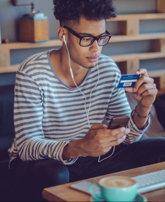 man in a striped shirt gazes at his tablet with a credit card in hand, indicating he might be reading about investing for beginners.