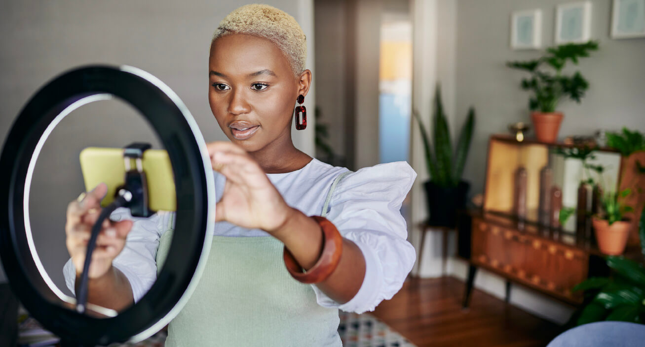 A Black woman sets up her phone in front of a round light, indicating she might be YouTuber and knows just how much do YouTubers make.