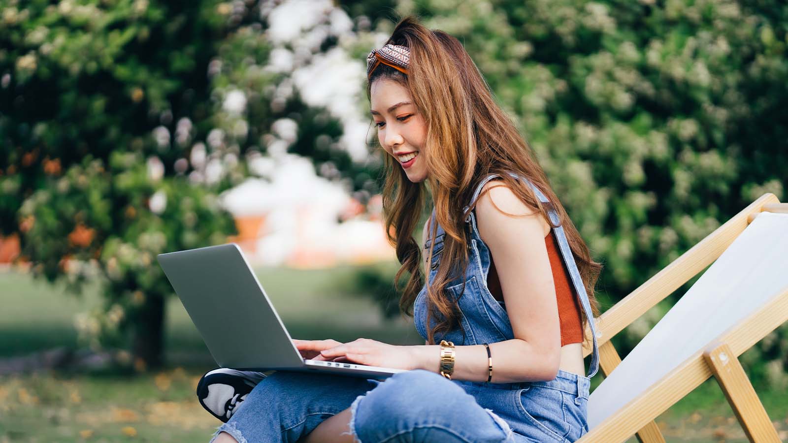 A college student sits outside, combing through student loan debt statistics on her laptop.