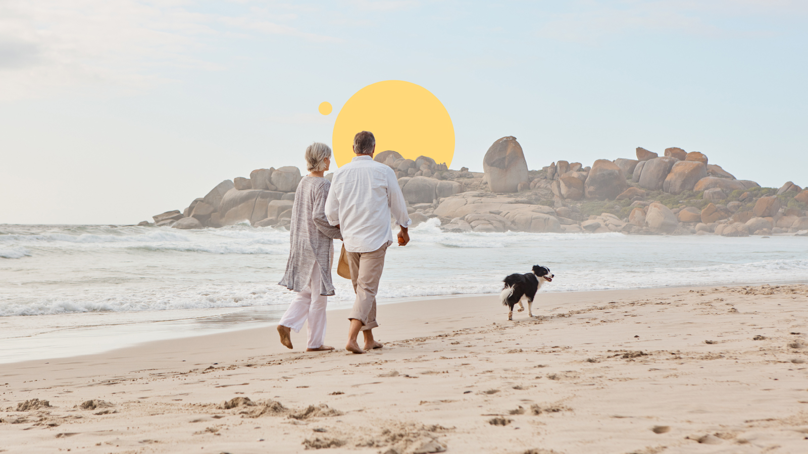 An older couple walking a dog along the beach